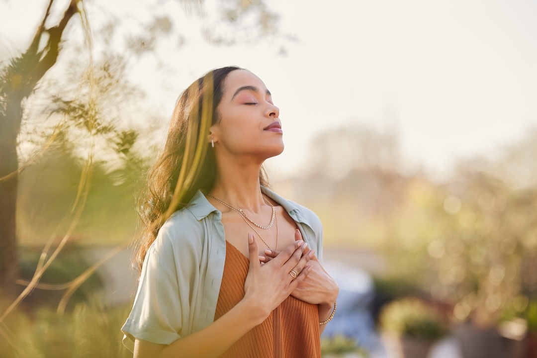 A person stands outside with their hands on their chest while taking a deep breath in