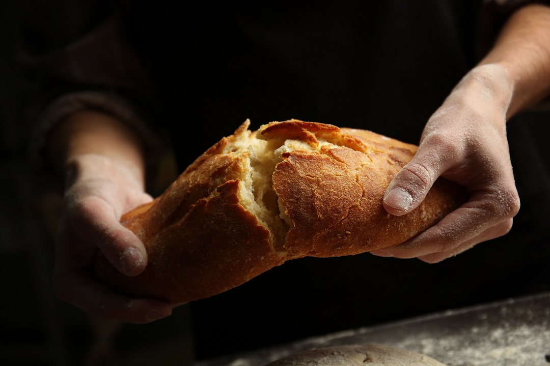 two hands breaking loaf of bread