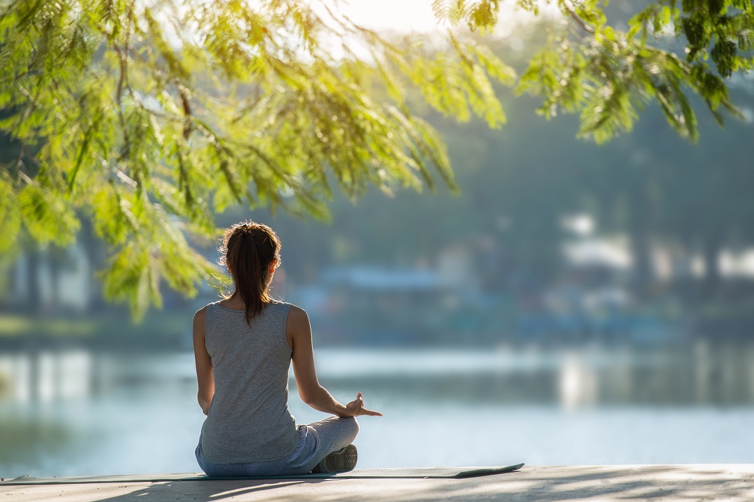 woman sitting cross-legged by lake, meditating