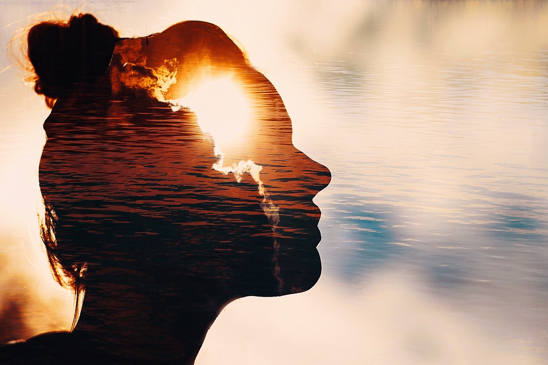 silhouette of contemplative woman, sun and water in background