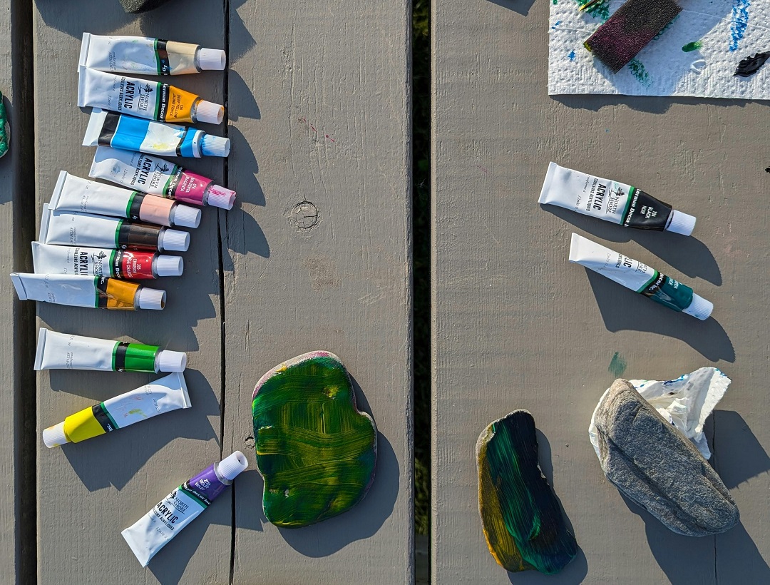 rocks and tubes of paint on wooden platform