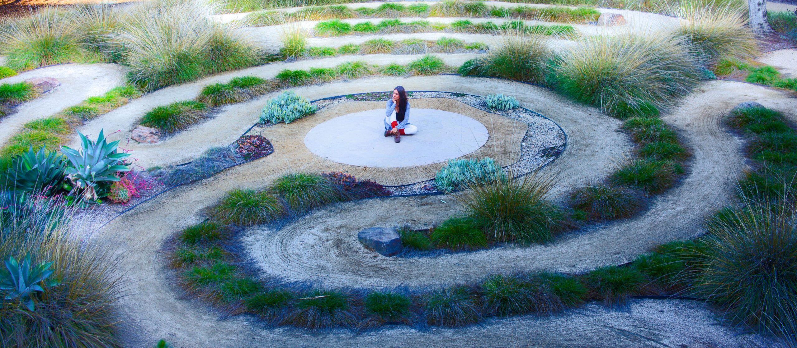 woman sitting in center of outdoor labyrinth, in contemplative pose