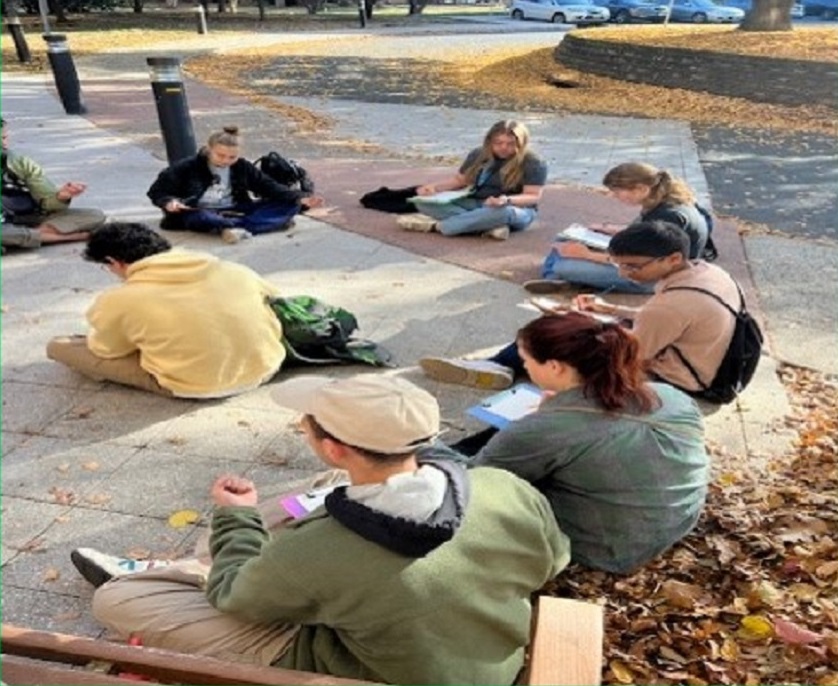 Group of people sitting outdoors, writing in their journals