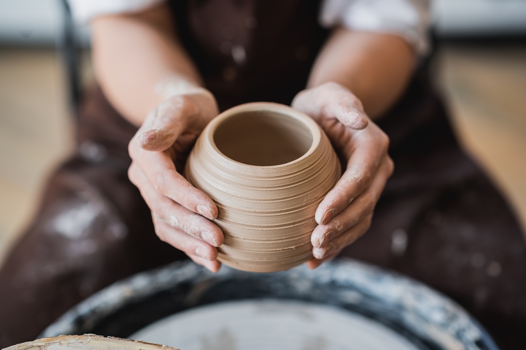Image of a person's hands shaping a piece of clay into a small beige pot or vase.