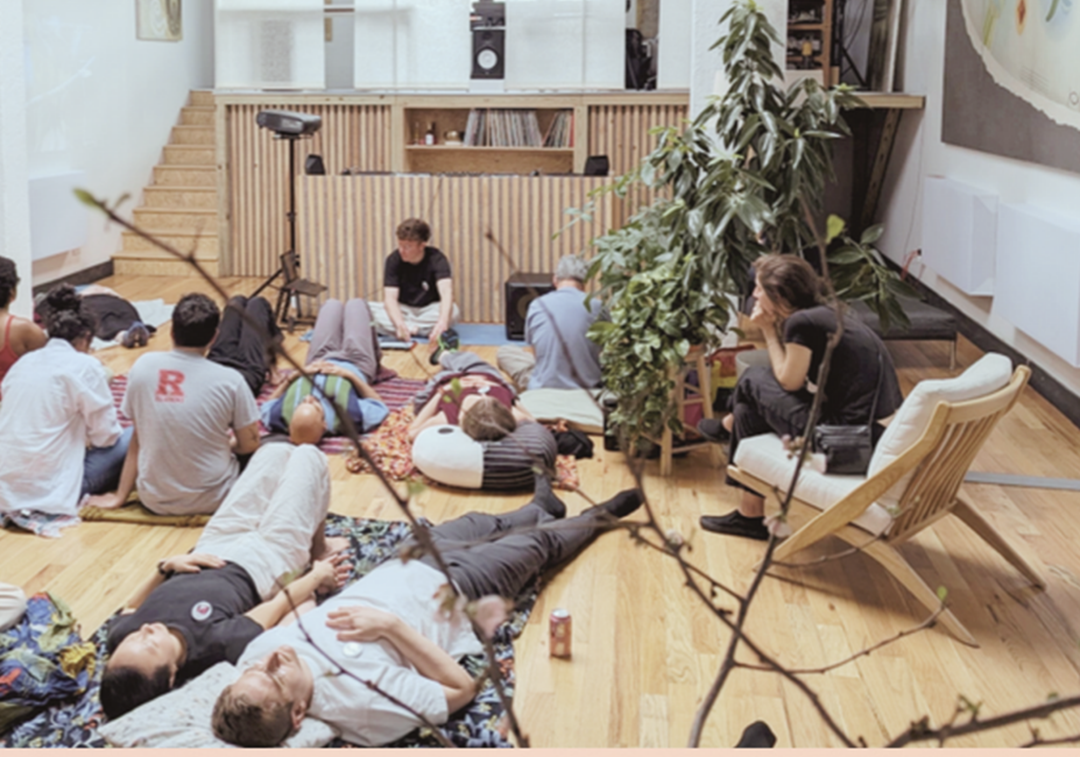 Image of a group of adults sitting or laying on a wood floor, being led through a listening activity