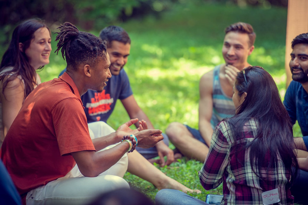 Group of six students sitting on grass having conversation. Mixture of genders and ethnicities