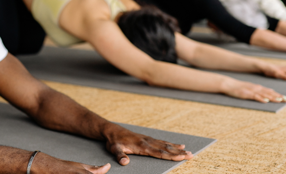 Image of a few people in a childs pose on yoga mats with both hands stretched out in front of them on the floor