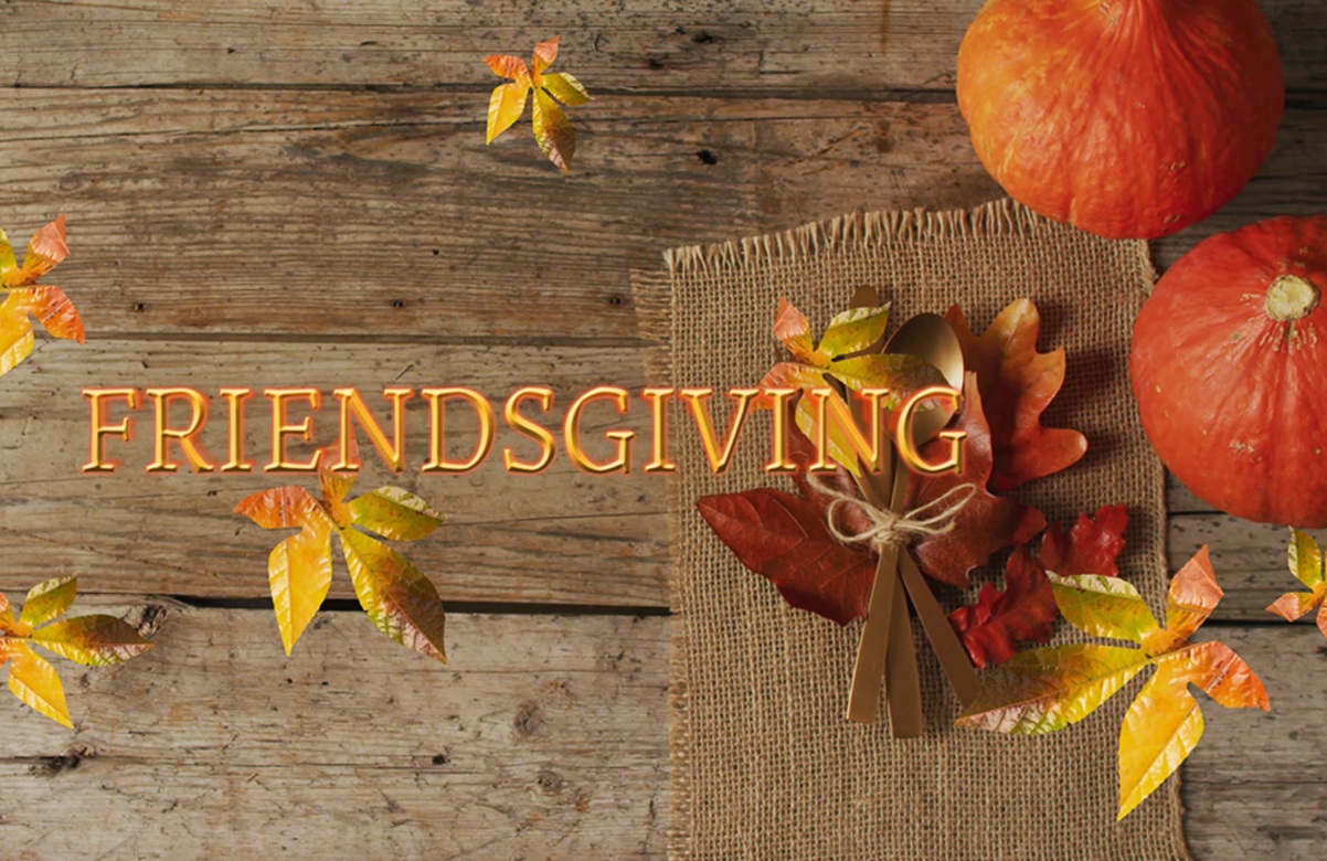 Photo of a wooden table with leaves and pumpkins on it, and the word "Friendsgiving" in orange font