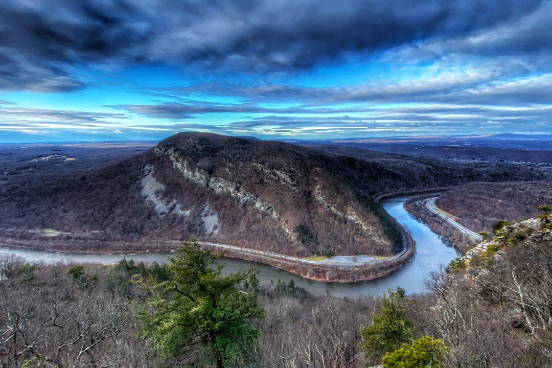 Overhead view of Mount Tammany, featuring a large mountain with a river running next to it and blue sky with clouds in background