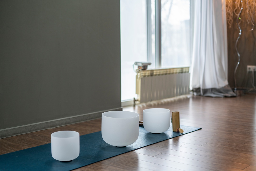 Image of a room with three different size crystal bowls on a mat on the floor, to be used for a sound bath.
