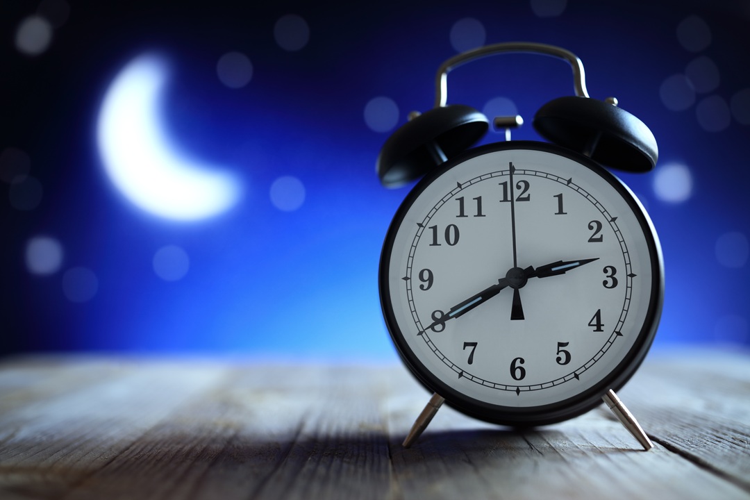 Image of an alarm clock on a wooden surface with a night sky and moon in the background. The clock is showing the time as 2:40 am