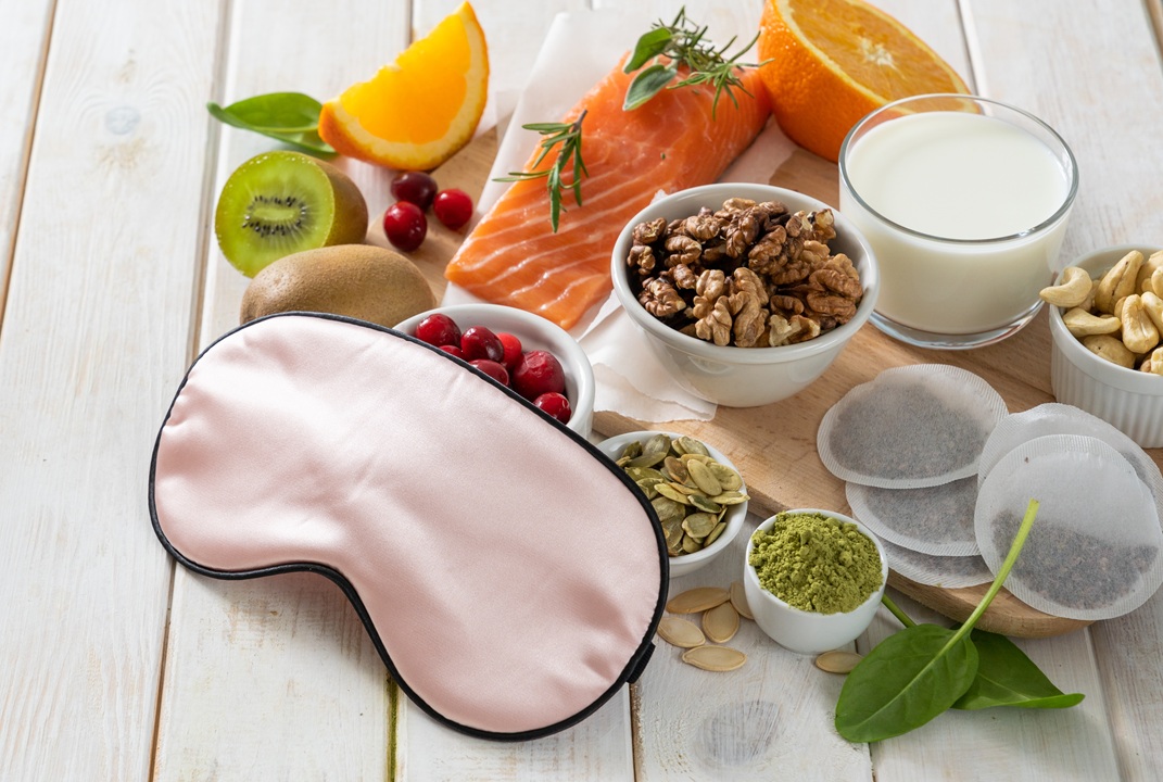 Photo of nutrition-filled foods like fruits, nuts, salmon and a pink sleep mask on a wooden surface