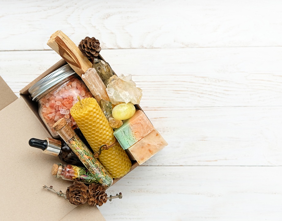 Photo of a collection of skin care items, including bath crystals in mason jar, soaps and a beeswax candle, all laying on a wooden surface.