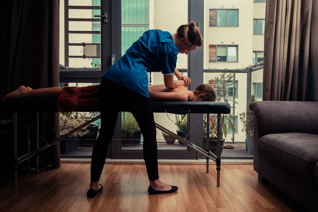 Photo of a woman giving a person a massage on table with large windows and view of buildings in the background