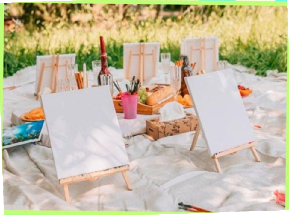 Photo of small wooden easels and art supplies set up on a white sheet on the grass in an open space