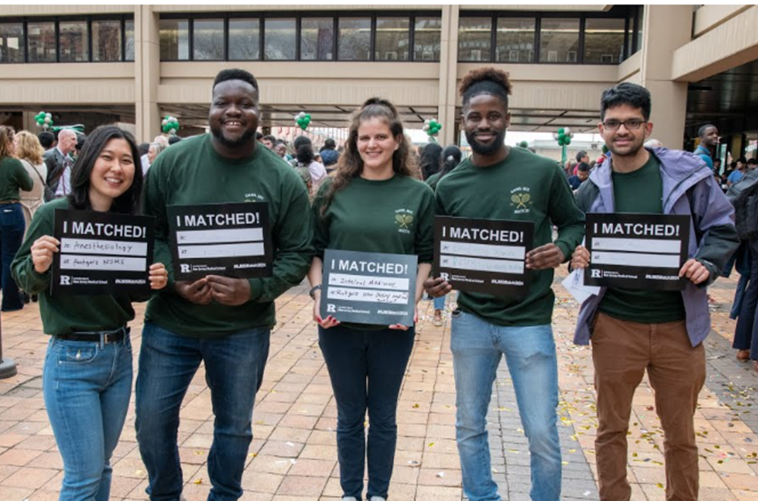 Five students standing in the Medical Sciences Building courtyard, each holding a sign stating the medical school at which they will do their residency