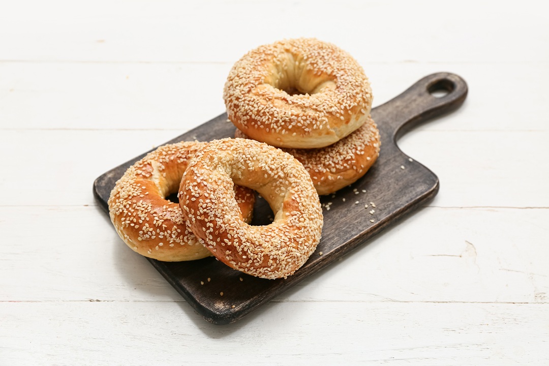 Photo of four sesame seed bagels on a wooden cutting board, white wood background