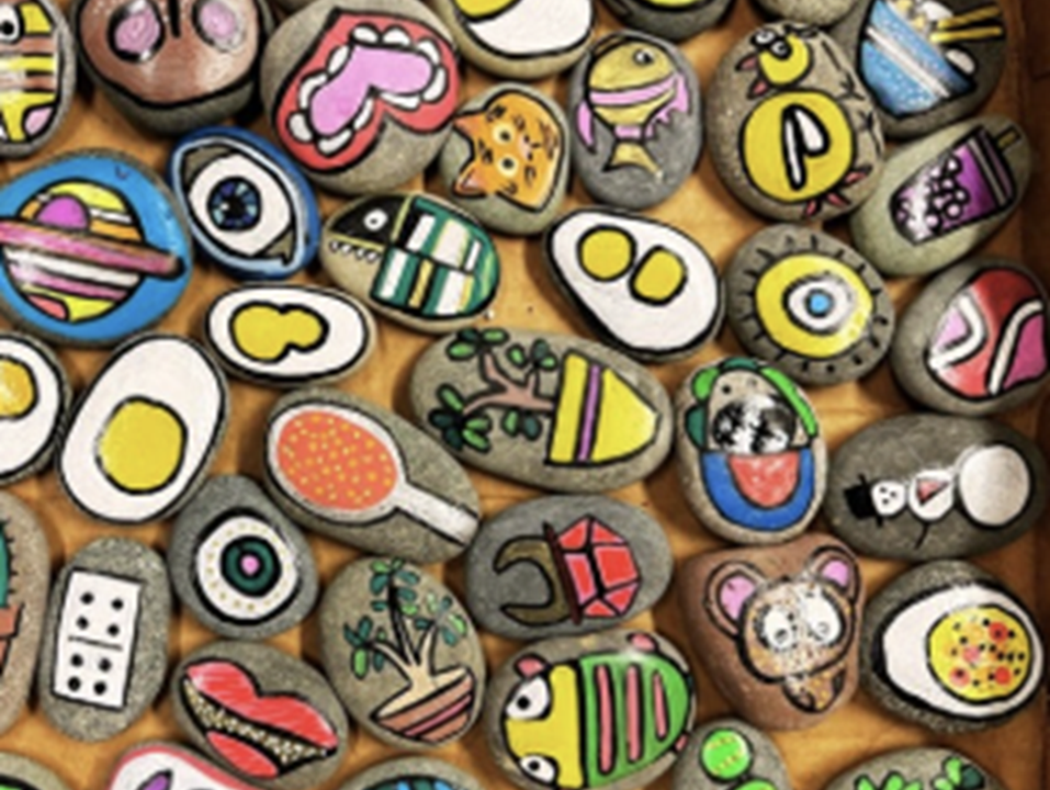 Image of several small flat rocks painted in bright colors, on a tan background