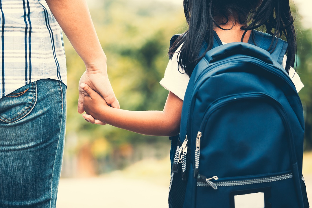 Photo of a woman and child with backpack walking away holding hands