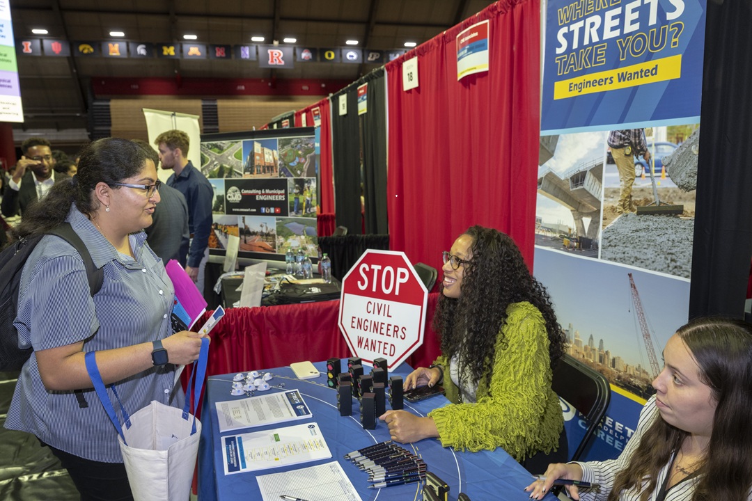 Photo of a young lady stopping at a table for information on a college course or other offering.