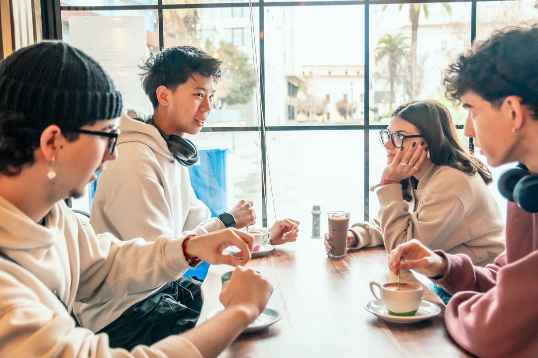 Group of 4 college students talking while sitting at a table with cups of coffee