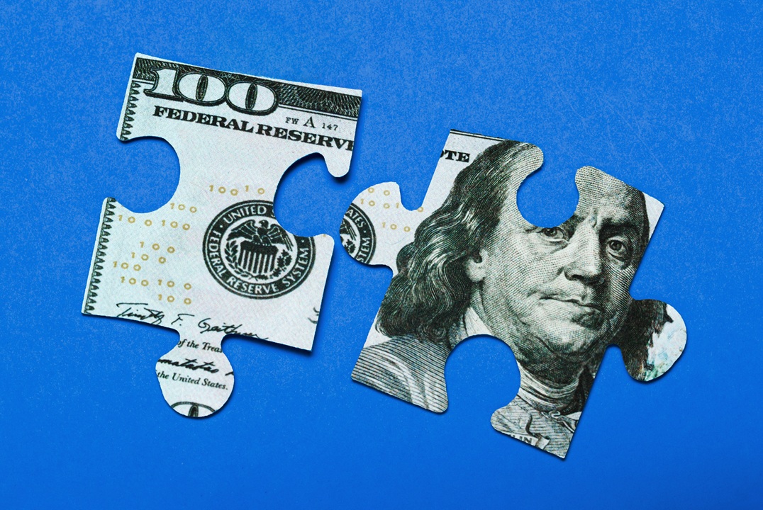 Image of two puzzle pieces with an image of a $100 bill on them, blue background