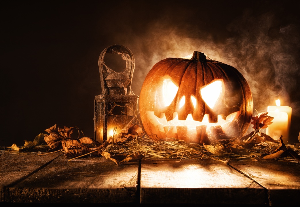 Spooky image of a pumpkin that has a carved face and is lit up, with dark background