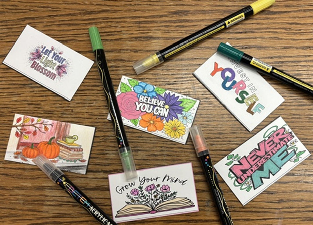 Photo of a wooden table with materials for making magnets on it - markers and white rectangles with colorful drawn images on them.